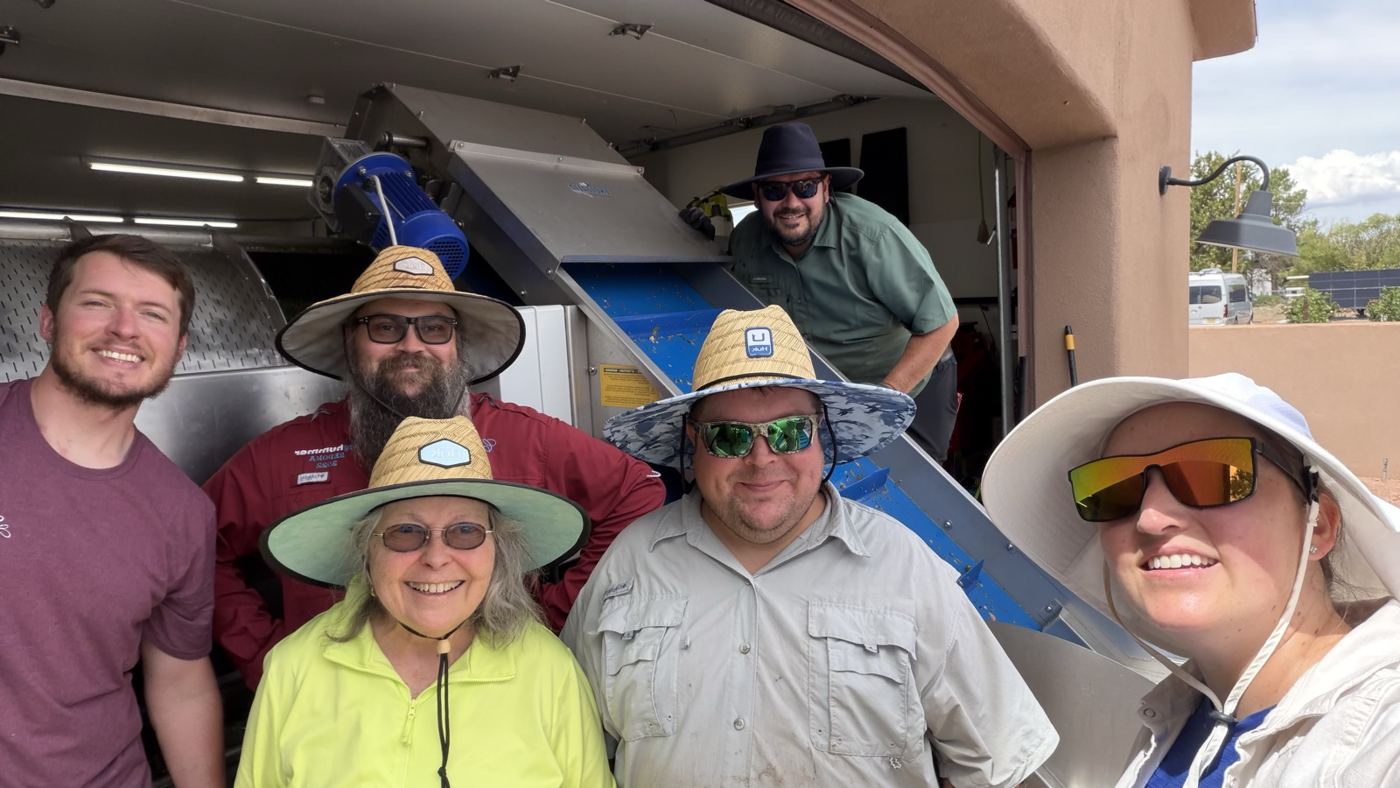 Six smiling crew members in sun hats at the crush pad